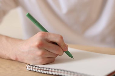 Ahşap masada kalemle not defterine yazan adam, yakın plan.