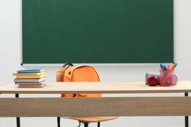 Farklı okul kırtasiyesi ve kırmızı elma, kapalı alanda tahtaya yakın ahşap masada.