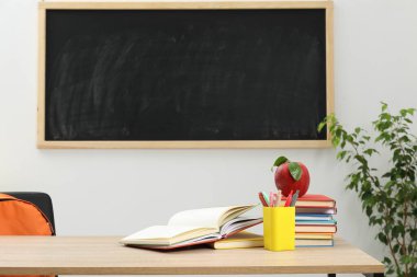 Farklı kırtasiye malzemesi ve kırmızı elma, kapalı alanda, tahtanın yanında.