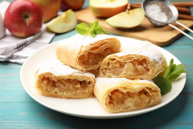 Lezzetli elmalı turta parçaları pudra şekerli ve nane şekerli açık mavi ahşap masa, yakın plan.