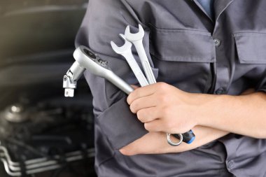 Otomobil parçaları. Kaputu açık, kapalı kaputun yanında anahtarı olan profesyonel bir tamirci, yakın plan. Metin için boşluk