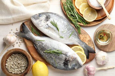 Taze çiğ dorado balığı, limon dilimleri, biberiye ve baharatlar beyaz ahşap masa, düz yatak. Organik deniz ürünleri