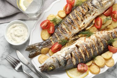 Beyaz mermer masada patates, domates, sos ve limonla servis edilen kızarmış deniz kabuğu balığı. Ev yapımı deniz ürünleri yemeği.