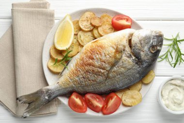 Lezzetli kavrulmuş dorado balığı, sebze ve sos ile servis edilir, beyaz ahşap masa üzerinde, düz yatar. Ev yapımı deniz ürünleri yemeği.