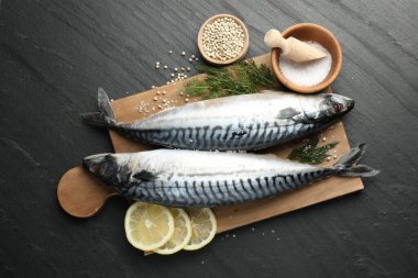 Taze çiğ uskumrular ve baharatlar siyah masada, düz yerde. Deniz ürünleri lezzetleri.