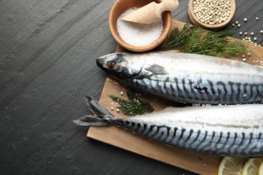 Deniz ürünleri lezzetleri. Taze çiğ uskumrular ve baharatlar siyah masada, düz yerde. Metin için boşluk