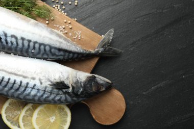 Deniz ürünleri lezzetleri. Taze çiğ uskumrular ve baharatlar siyah masada, düz yerde. Metin için boşluk