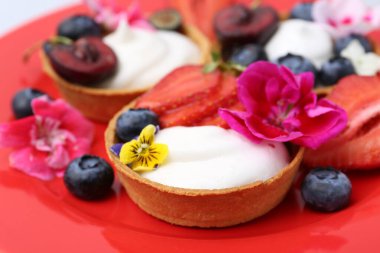 Kırmızı tabakta böğürtlenli turtalar ve çiçekler, yakın plan. Tatlı nefis.