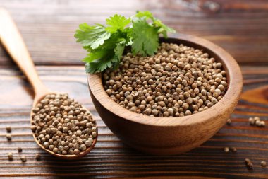 Kişniş tohumları ve taze kişniş yaprakları ahşap masada, yakın plan.