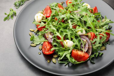 Lezzetli salata roka, mozzarella ve sebzeler gri masada, yakın plan.