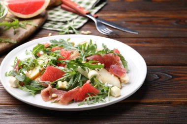 Lezzetli salata roka, prosciutto, peynir, armut, greyfurt ve ahşap masada fındık, yakın plan.