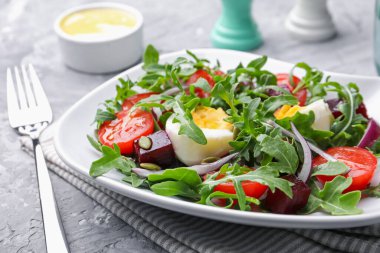 Lezzetli salata roka, sebze ve yumurta gri masada servis edilir, yakın plan.