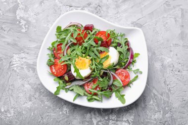 Lezzetli salata roka, sebze, yumurta ve tohumlar gri masada, üst manzara.