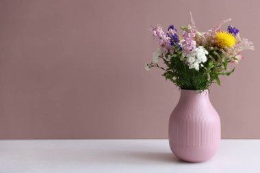 Beyaz masadaki vazodaki güzel çiçekler pembe arkaplana karşı, metin için boşluk
