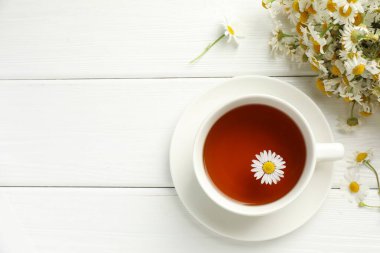 Bardakta Aromatik çay ve beyaz ahşap masada papatya çiçekleri, düz yatış. Metin için boşluk