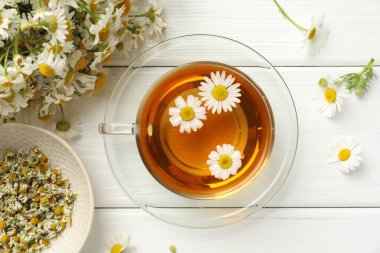 Cam bardakta Aromatik çay ve beyaz ahşap masada papatya çiçekleri.
