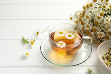 Cam bardakta Aromatik çay ve beyaz ahşap masada papatya çiçekleri, yakın plan.