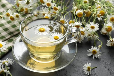 Lezzetli papatya çayı ve çiçekler siyah masada, yakın plan.