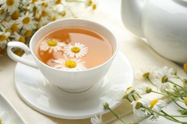 Lezzetli papatya çayı ve çiçekler beyaz ahşap masada, yakın plan.