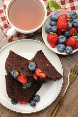 Tahta masada servis edilen çilekli ve yaban mersinli çikolatalı kek parçaları.
