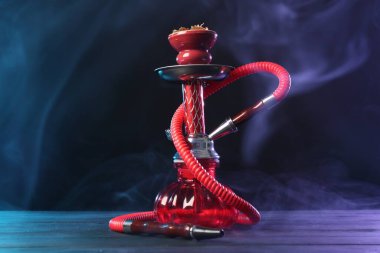 Siyah arka planda sigara dumanı olan ahşap masada nargile.