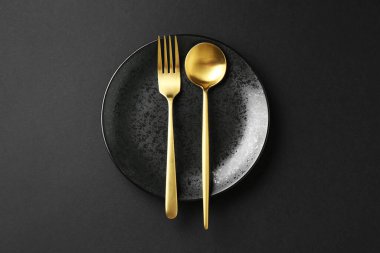 Siyah arka planda şık tabak ve çatal bıçak takımı, üst görünüm
