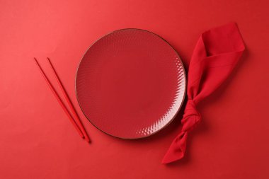 Şık bir tabak, yemek çubukları ve kırmızı arka planda peçete.