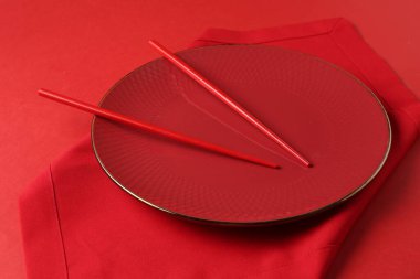 Kırmızı arka planda şık tabak, çubuk ve peçete, yakın plan.