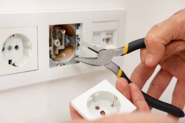 Kapalı mekanda penseyle prizleri tamir eden adam, yakın plan.