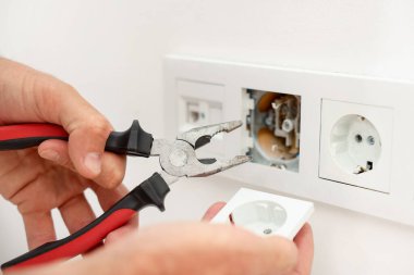 Kapalı mekanda penseyle prizleri tamir eden adam, yakın plan.