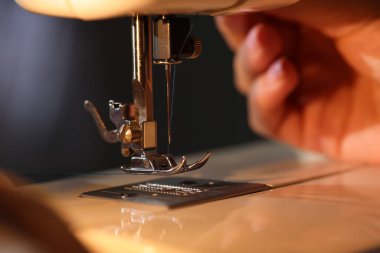 Bulanık gri arkaplan ve makro görünüm üzerinde dikiş makinesiyle çalışan kadın