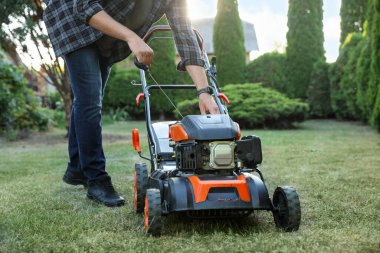 Bahçedeki çim biçme makinesinin marş kablosunu çeken adam, yakın plan.