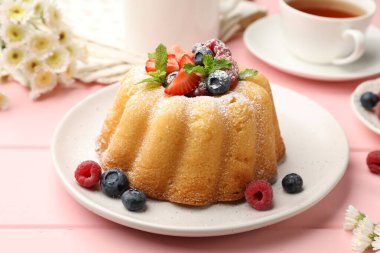 Pudra şekerli, böğürtlenli ve nane şekerli nefis kek, pembe ahşap masa, yakın plan.