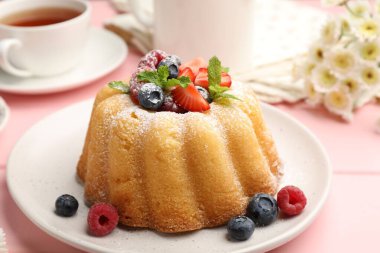 Pudra şekerli, böğürtlenli ve nane şekerli nefis kek, pembe ahşap masa, yakın plan.