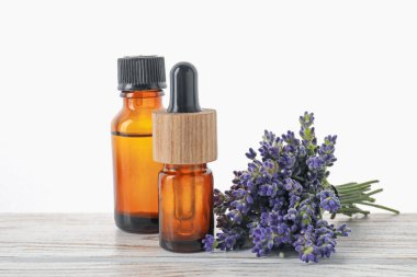 Beyaz arka plana karşı ahşap masa üzerinde doğal yağ ve lavanta çiçekleri