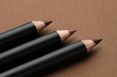 Kahverengi arka planda farklı kaş kalemleri, yakın plan.