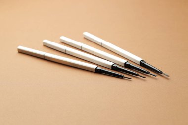 Kahverengi arka planda otomatik kaş kalemleri, yakın plan.