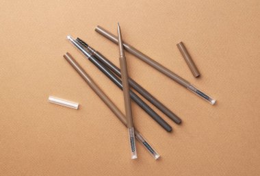 Kahverengi arka planda farklı kaş kalemleri, düz yatış.