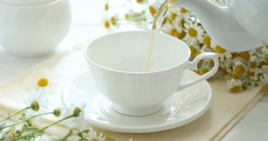 Lezzetli papatya çayını beyaz ahşap masaya dökerek, yakın plan.