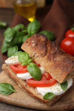 Mozarella peynirli, domatesli ve ahşap masadaki fesleğenli lezzetli sandviç.
