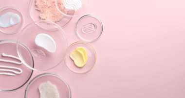 Petri kaplarında pembe arka planda farklı kozmetik ürünleri var. Metin için boşluk