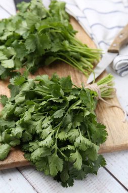 Tahta kesme tahtası taze kişniş ve bıçak beyaz ahşap masada, yakın plan.