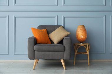 Açık mavi duvarın yanında rahat bir koltuk ve lamba.