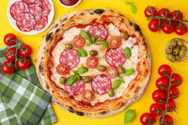 Lezzetli pizza ve malzemeler sarı masada, düz yerde.