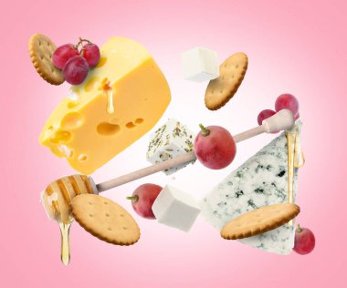 Peynir tahtası ürünleri pembe gradyan arka planda havada. Farklı peynir, üzüm, kraker ve bal çeşitleri.