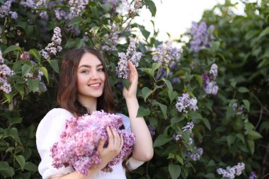 Leylak çiçeklerinin arasında gülümseyen ve açık havada terk eden kadın.