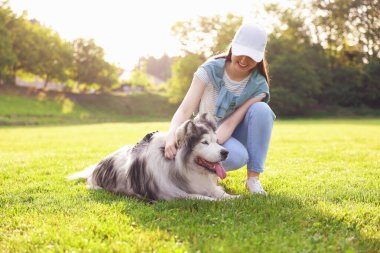 Gülen kadın ve sevimli Alaska köpeğiyle açık havada yeşil çimlerin üzerinde