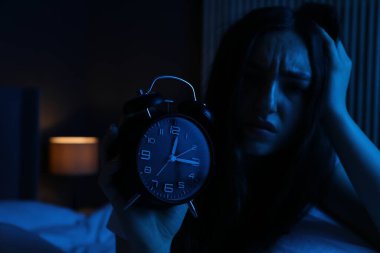Evde yatağında uykusuzluk çeken, çalar saati olan hayal kırıklığına uğramış bir kadın.