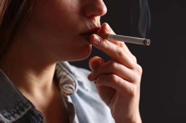 Arka planda sigara içen tişörtlü bir kadın, yakın plan. Kötü alışkanlık.