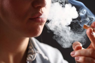 Arka planda sigara içen tişörtlü bir kadın, yakın plan. Kötü alışkanlık.